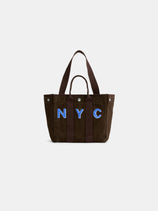 The Perfect Daily Tote is a brown cotton bag with two sturdy handles, showcasing bold blue “NYC” lettering on the front and set against a plain white background. Combining style and practicality, this personalized tote is ideal for everyday use.
