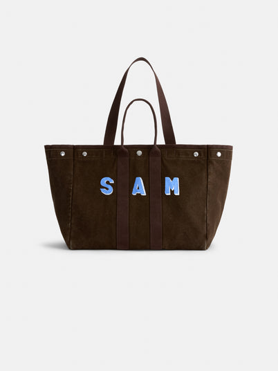 Sure! Here’s your rewritten sentence using the provided product data: A brown suede Painted Perfect Weekend Tote with dark handles and the name SAM in large blue and white letters on the front, displayed on a plain white background—this Alex Mill tote is perfect for those seeking stylish, monogrammable bags that make a personal statement.