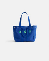 Introducing The Perfect Weekday Tote: a blue cotton bag with two sturdy handles, front snap buttons, and the letters B G K elegantly embroidered in green and white on the front—ideal for anyone who loves personalized accessories or is searching for a monogrammable tote bag.