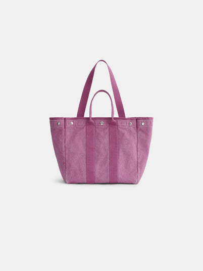 A pink cotton tote bag called The Perfect Weekday Tote, featuring two short handles, a long shoulder strap, and silver rivet accents, is displayed against a plain white background. This versatile bag combines classic style with functionality.
