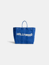 The Collector’s Weekday Tote Hollywood is a spacious blue canvas bag featuring two handles and bold white “HOLLYWOOD” lettering on the front.