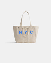 Introducing The Perfect Weekday Tote: crafted from beige cotton with sturdy double handles, this chic accessory showcases bold NYC lettering in blue across the front and is finished with silver rivets at the top corners. Ideal for daily use, it’s also part of our monogrammable tote bag collection—so you can personalize it to make it truly one-of-a-kind.