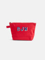 The Painted Perfect Canvas Pouch is a red zippered bag with a small side handle, featuring the embroidered initials BJW in blue and white on the front—a stylish personalized accessory perfect for use as a makeup bag.