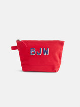 The Painted Perfect Canvas Pouch is a red zippered bag with a small side handle, featuring the embroidered initials BJW in blue and white on the front—a stylish personalized accessory perfect for use as a makeup bag.