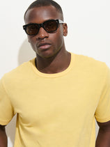 A man wearing black sunglasses and The Standard T-Shirt In Slub Cotton in yellow stands against a plain white background, looking directly at the camera with a neutral expression.