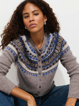 A woman with curly hair models the Charlotte Fairisle Sweater in Wool, featuring a blue, white, and brown vintage Fair Isle yoke. She sits against a white background, looking directly at the camera with a neutral expression.